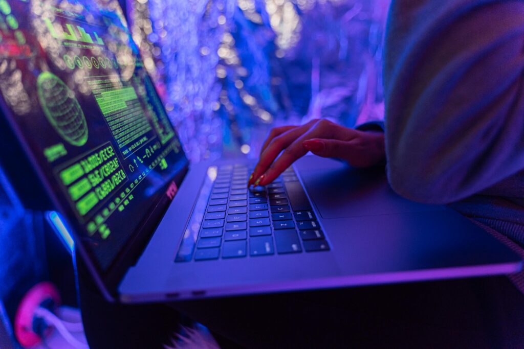 pexels-photo-5475752-5475752-1 Close-up of hands typing on a laptop displaying cybersecurity graphics, illuminated by purple light.